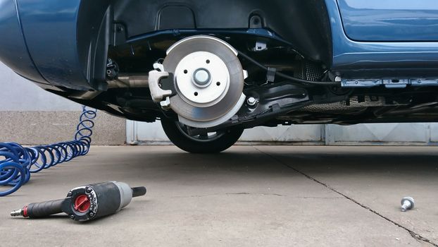 View of a car disc brake and pneumatic air screwdriver on the ground during tyre replacement. Car maintenance.