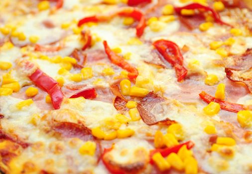 A closeup of pizza surface with ham, salami, cheese and red pepper. Full frame background shot of pizza, selective focused on foreground.