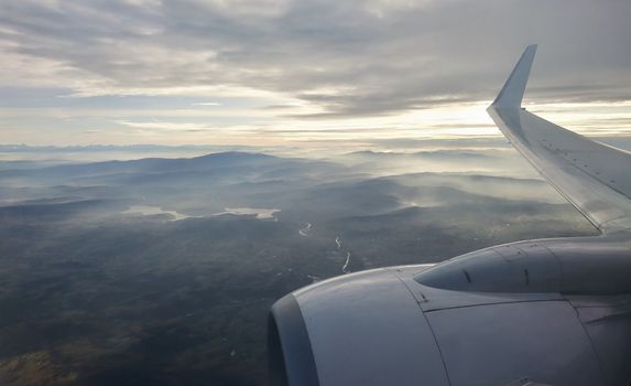 View through window over wing and engine during flight. View of country and mountains from plane during landing.