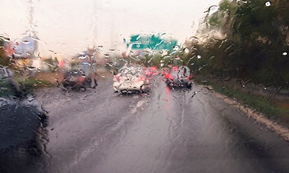 Driving a car in the rain and storm in heavy traffic. View through a windshield with rain drops during driving a car. Shallow depth of field.