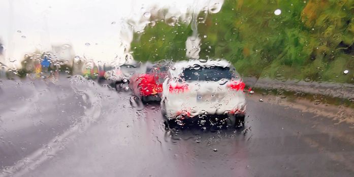 Driving a car in the rain and storm in heavy traffic. View through a windshield with rain drops during driving a car. Shallow depth of field.