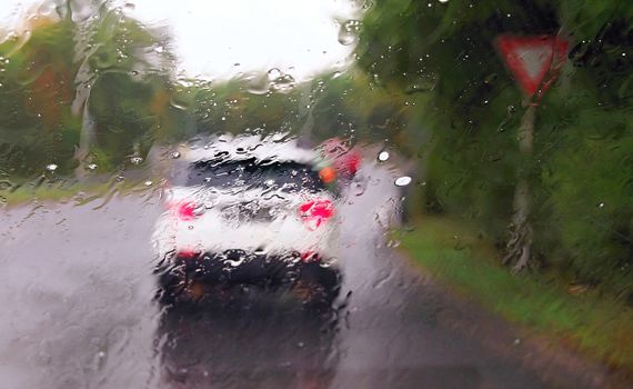 Driving a car in the rain and storm in heavy traffic. View through a windshield with rain drops during driving a car. Shallow depth of field.