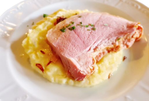 Roast ham slice with mashed potatoes on white plate.
