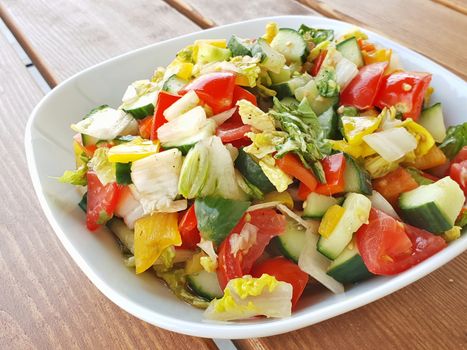 Closeup of fresh vegetable salad in a white bowl on wooden plank background.