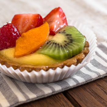 A cake with cream and mixed fruit, resting on linen tablecloth.