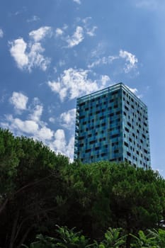 A skyscraper with modern style emerges from a group of trees.