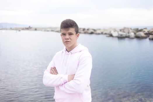 Young teenager with crossing arms standing on promenade while looking at camera