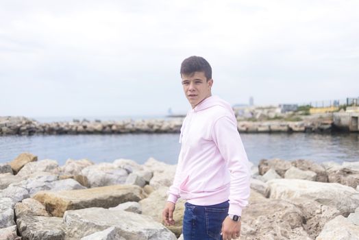 Young teenager standing on rock breakwater while looking at camera