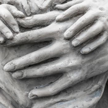 Detail of a marble statue with hands of child and woman together.