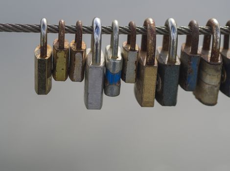 close up colorful locks hanging from high wire of bridge on light gray background