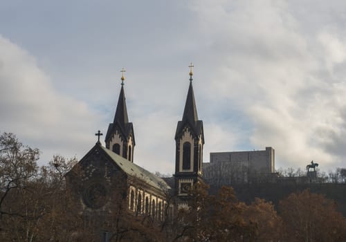 Saints Cyril and Methodius gothic church and National Monument at Vitkov with Equestrian Statue of Jan Zizka viewed from Karlinske namesti square park with late autumn trees. Czech Republic, Prague.