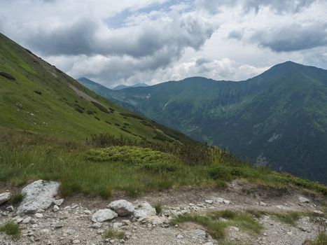Beautiful mountain landscape with lush green grass, dwarf scrub pine and bare mountain peaks. Ziarska dolina, Western Tatras mountains, Rohace Slovakia, summer dramatic clouds sky background.