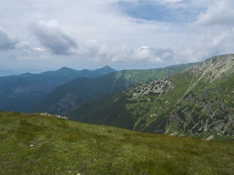 Beautiful mountain landscape with lush green grass, meadow and bare mountain peaks on ridge Western Tatras mountains, Rohace Slovakia, summer dramatic clouds sky background.