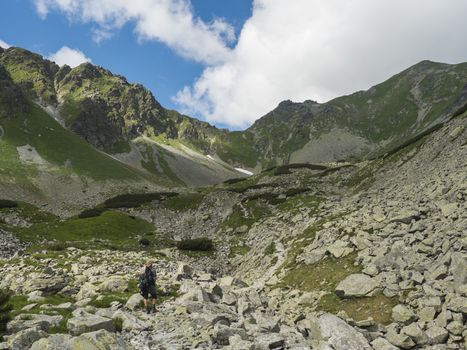 Man hiker with hat and backpack hiking footpath trail in mountain valley Smutna dolina with rock boulders, dwarf scrub pine and green mountain peaks. Western Tatras mountains, Rohace Slovakia, summer, blue sky background