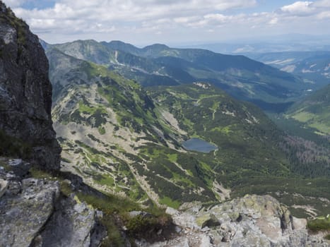 Beautiful vivid blue mountain lake Rohacske pleso with green mountain peaks and hiking path. view from the Ostry rohac, Western Tatras mountains, Rohace Slovakia, summer sunny day blue sky.