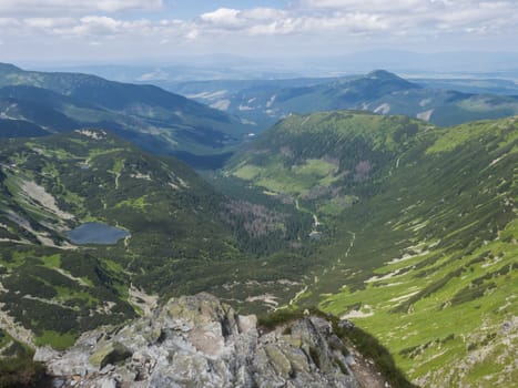 Beautiful vivid blue mountain lake Rohacske pleso with green mountain peaks and hiking path. view from the Ostry rohac, Western Tatras mountains, Rohace Slovakia, summer sunny day blue sky.