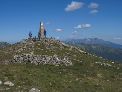 Slovakia, Western Tatra mountain, July 4, 2019: group of hiker people resting on top of Baranec peak in Western Tatra mountains with Rohace panorama. Sharp green mountains with hiking trail on ridge. Summer blue sky background.