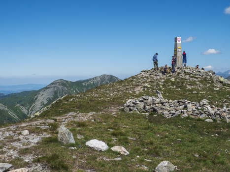 Slovakia, Western Tatra mountain, July 4, 2019: group of hiker people resting on top of Baranec peak in Western Tatra mountains with Rohace panorama. Sharp green mountains with hiking trail on ridge. Summer blue sky background.