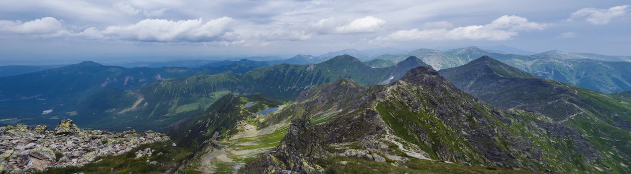 Panoramic view from Rohac peak on Western Tatra mountains or Rohace panorama with hiking trail on ridge. Sharp green mountains and mountain lakes Jamnicke plesa. Summer blue sky white clouds