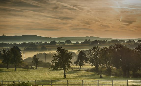 landscape in the nature of the begium hills with haze , mist and hills at the background with trees in the forground