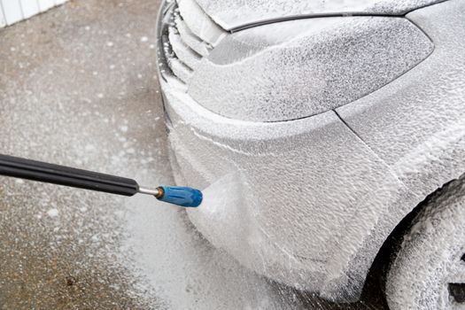 A closeup view of process of indoor wet car washing. Front side with headlamp. Applying soap sud.