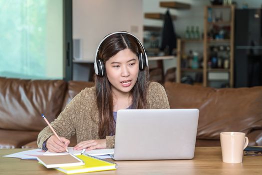 Asian business woman using technology laptop and headphone for working from home in indoor house by video conference call, startups and business owner, social distance and self responsibility