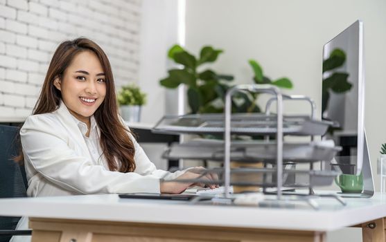 Asian business woman working and typing keyboard of technology computer in happy action at office desk, startup and entrepreneur, businessperson and small business concept