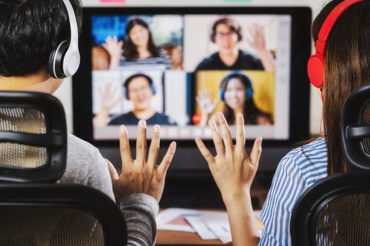 Rear View of Asian Business people say hello with teamwork colleague in video conference when Coronavirus outbreak, Covid-19 pandemic, online meeting, Social distancing and new normal concept