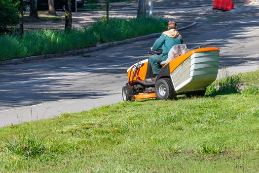 A utility worker using a professional lawn mower mows tall grass along the side of a city road on a clear sunny day, copy space.