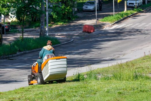 A utility worker takes care of roadside lawns, mowing tall grass with a professional lawnmower, image with copy space.