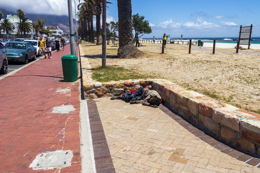 Poor homeless man sleeps on the street in the heat in Camps Bay, Cape Town, South Africa.