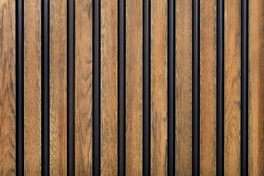 A wooden fence made of vertical decorative planks with a pronounced texture of light brown color with black spaces.