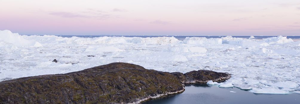 Greenland landscape nature with icebergs and ice in Greenland icefjord. Aerial drone panoramic banner photo of Ilulissat Icefjord with icebergs from Jakobshavn Glacier. Person in image for scale.