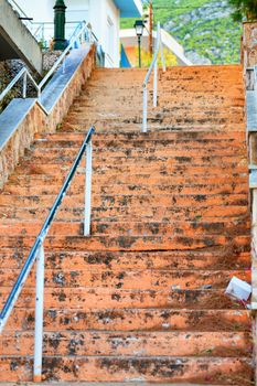 The shabby steps of an old stone staircase rise uphill and lead to the light under the bright sun on a narrow Greek street, selective focus.