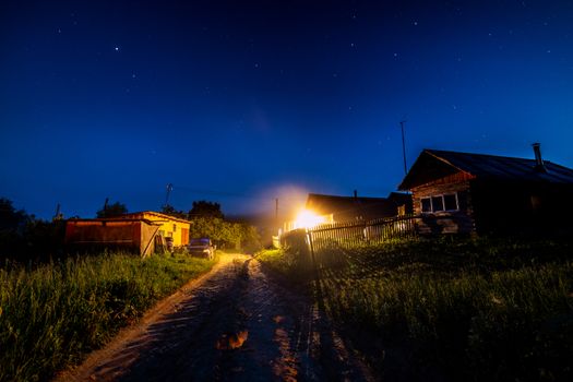 Starry night sky over village house in summer. Wooden house with one bulb light over entrance. Russia