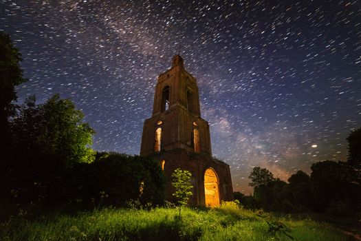 night brick bell tower ruin in forest at starry night with mystical internal light.