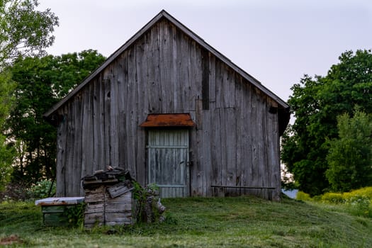 old wooden barn on yard with mowed lawn at summer evening.