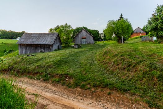 old wooden barns on yard with mowed lawn at summer evening.