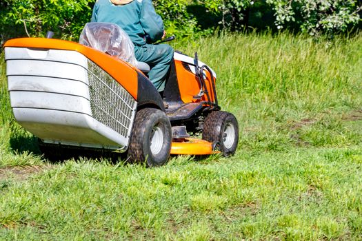 A well-kept park with a trimmed lawn as a result of a gardener working with a professional tractor lawn mower on a clear sunny day.