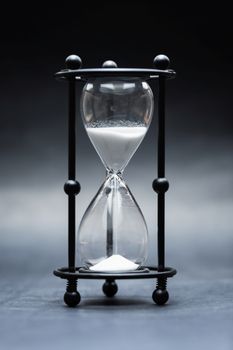 Hourglass with white sand against dark background closeup