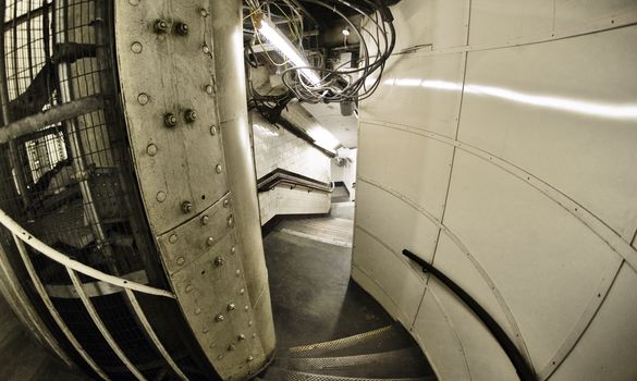 Wide angle fisheye lens shot of metal construction, cables and neon lights illuminating stairway leading down to Elephant and Castle undergroud station in London.