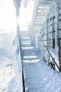 Snow and ice covered stairs and windows at top of mountain Chopok ski resort, with strong sun backlight in background illustrating extreme cold in the winter. Jasna, Slovakia.