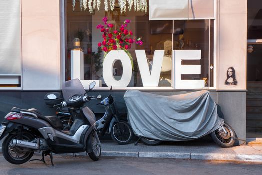 Concept of Love. Shop window with big letters LOVE , red flowers and motorbikes, motorcycle outdoor near the window. Conceptual photo. Love theme. Rock style background