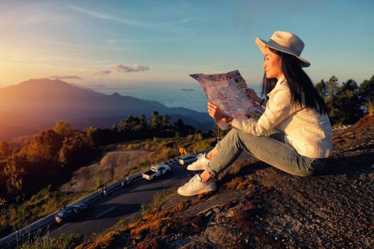 Happy woman reading a map siting on green grass meadow on top of mountain and enjoying nature ,sunrise in winter
