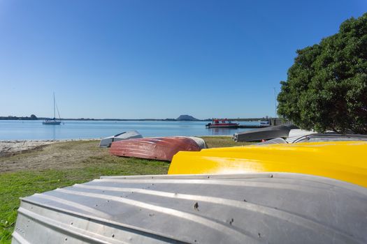 Omokoroa waterfront with with bright yellow hull among upturned dingies on beach and landmark Mount Maunganui in distance.