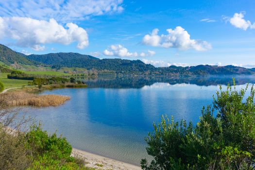 View across Lake Okareka to small lakeside village at base of distant hills.