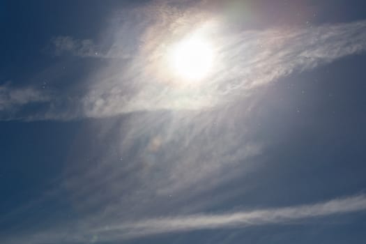 dust particles on blue sky with sun and feather cloud at spring day.