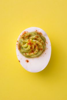 Stuffed egg with guacamole and paprika on yellow background