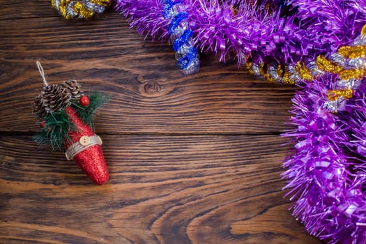 a christmas tree toy and purple tinsel on brown wood background - horizontal perspective