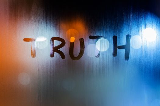 the word truth written on night wet window glass close-up with bokeh background.
